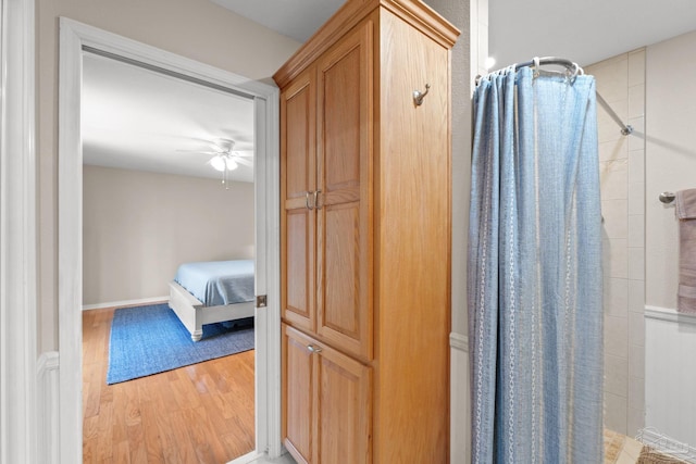 bathroom with ceiling fan, baseboards, wood finished floors, and tiled shower