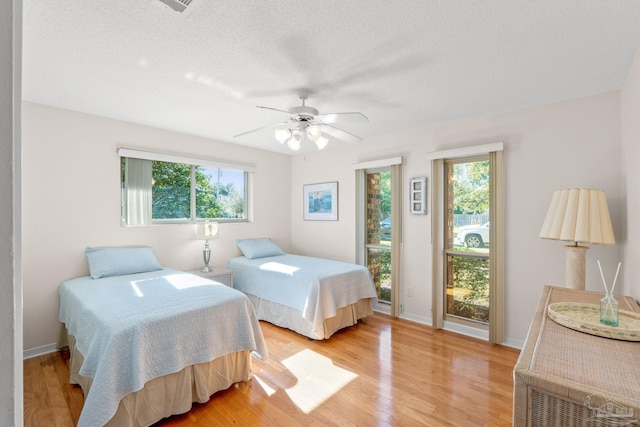 bedroom featuring access to exterior, light wood-style floors, ceiling fan, a textured ceiling, and baseboards