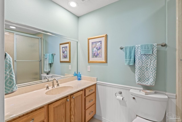 full bathroom featuring a shower with shower door, toilet, a wainscoted wall, recessed lighting, and vanity