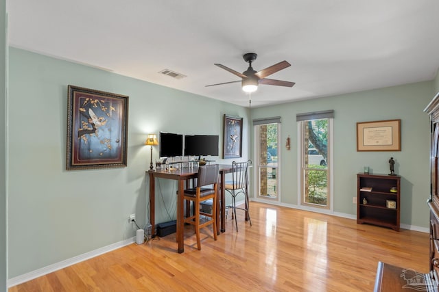 home office with a ceiling fan, visible vents, baseboards, and wood finished floors