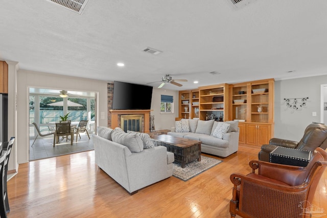 living area with light wood-type flooring, a brick fireplace, visible vents, and ceiling fan