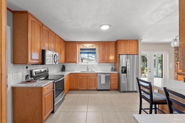 kitchen with light tile patterned floors, backsplash, stainless steel appliances, light countertops, and a sink