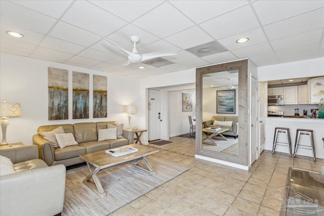 living room featuring ceiling fan, a drop ceiling, and light tile patterned flooring