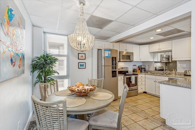 kitchen featuring hanging light fixtures, white cabinets, stainless steel appliances, and a drop ceiling