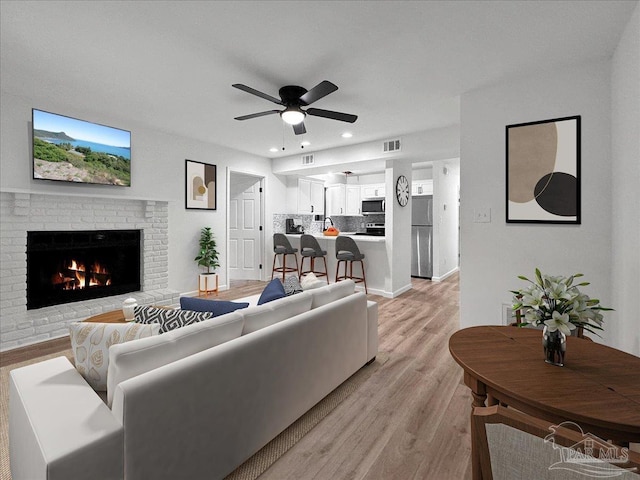 living room with ceiling fan, a brick fireplace, and light hardwood / wood-style flooring