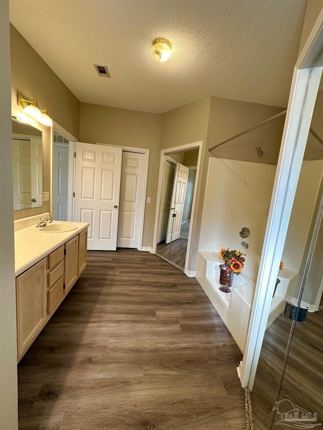 bathroom with hardwood / wood-style flooring, vanity, a bath, and a textured ceiling