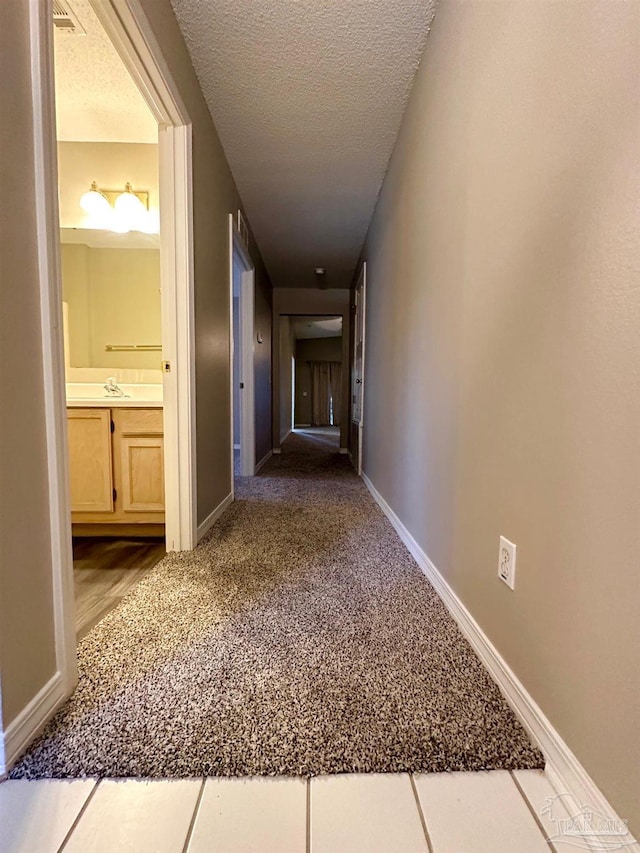 hallway featuring carpet floors, sink, and a textured ceiling