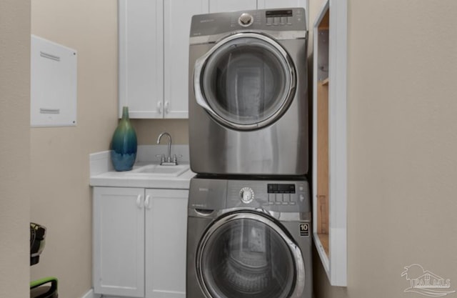 washroom with cabinets, stacked washer / dryer, and sink