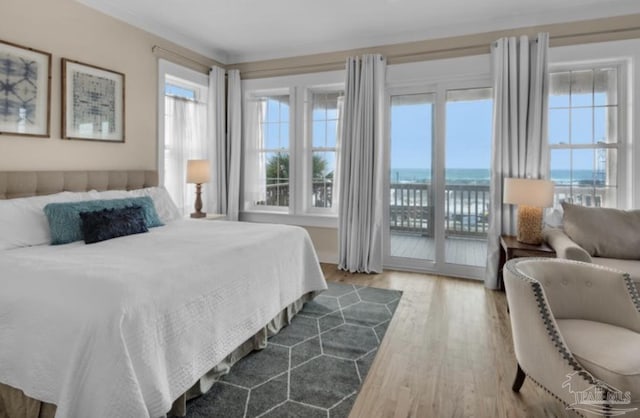 bedroom with access to exterior, a water view, multiple windows, and hardwood / wood-style flooring