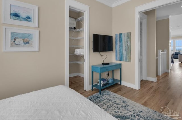 bedroom with hardwood / wood-style floors, a spacious closet, ornamental molding, and a closet