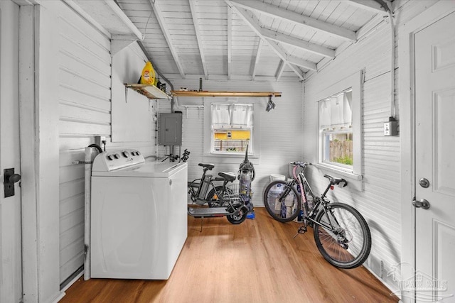 laundry area with washing machine and clothes dryer, electric panel, wood walls, and light hardwood / wood-style floors