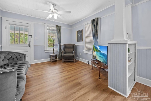 living area with ceiling fan, ornamental molding, wooden walls, and light hardwood / wood-style floors