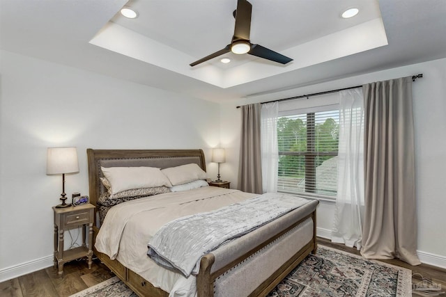 bedroom with ceiling fan, dark hardwood / wood-style flooring, and a tray ceiling