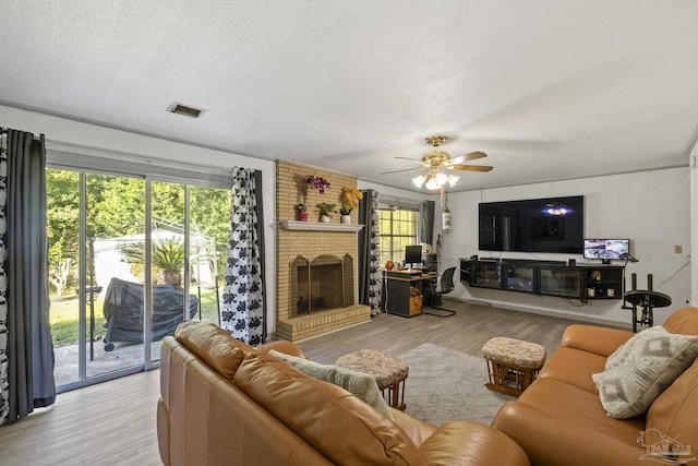 living room with ceiling fan, a fireplace, light hardwood / wood-style floors, and a textured ceiling