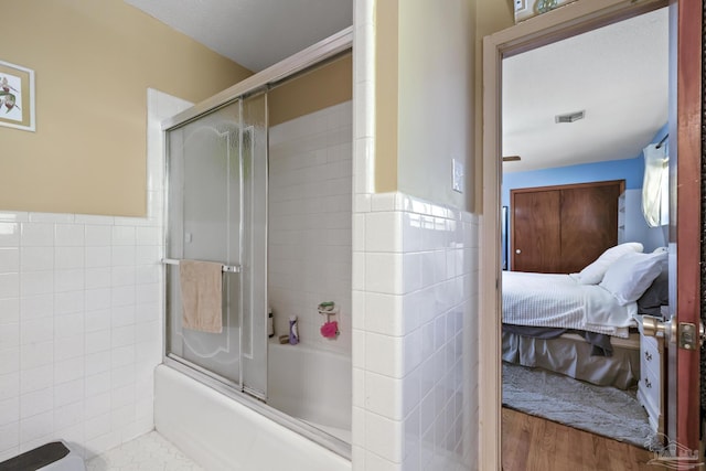 bathroom featuring hardwood / wood-style flooring, tile walls, and enclosed tub / shower combo