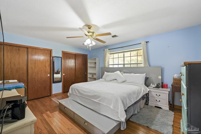 bedroom featuring a textured ceiling, ceiling fan, two closets, and light wood-type flooring