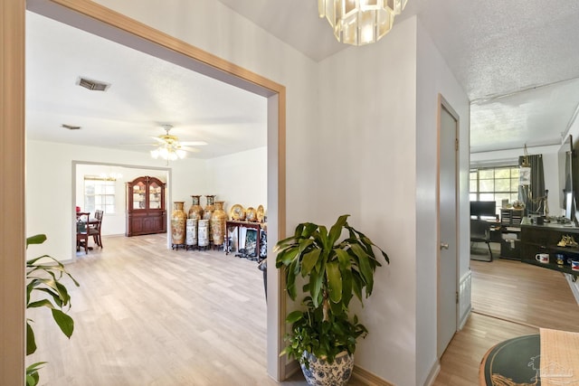 hall with a chandelier, light hardwood / wood-style floors, and a textured ceiling