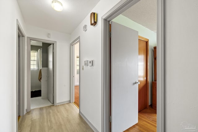 hallway with a textured ceiling and light hardwood / wood-style flooring