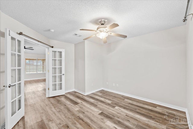 unfurnished room with ceiling fan, a textured ceiling, light wood-type flooring, and french doors