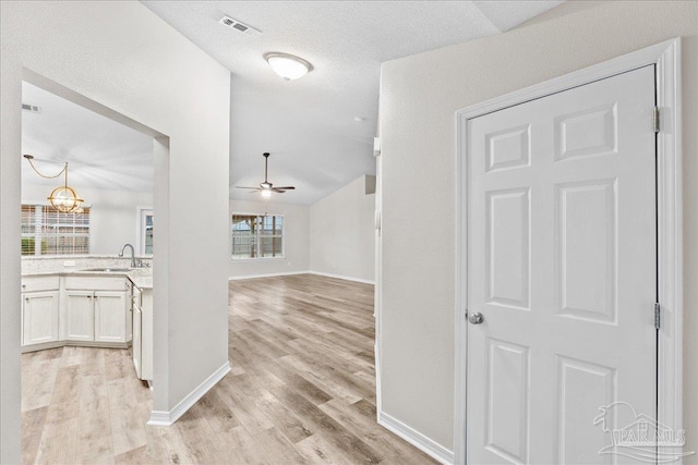 corridor featuring sink, an inviting chandelier, vaulted ceiling, a textured ceiling, and light wood-type flooring