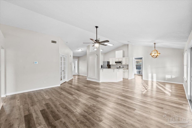 unfurnished living room featuring ceiling fan with notable chandelier, high vaulted ceiling, and light hardwood / wood-style floors