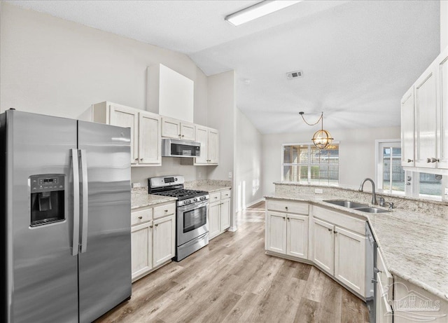 kitchen featuring appliances with stainless steel finishes, pendant lighting, lofted ceiling, sink, and light wood-type flooring