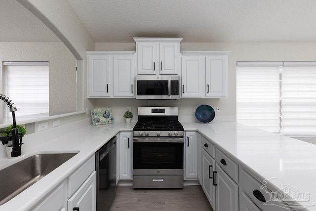 kitchen with dark hardwood / wood-style floors, white cabinetry, sink, stainless steel appliances, and a textured ceiling