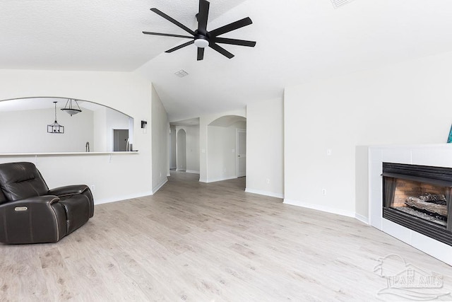 living room featuring a tiled fireplace, ceiling fan, lofted ceiling, and light wood-type flooring