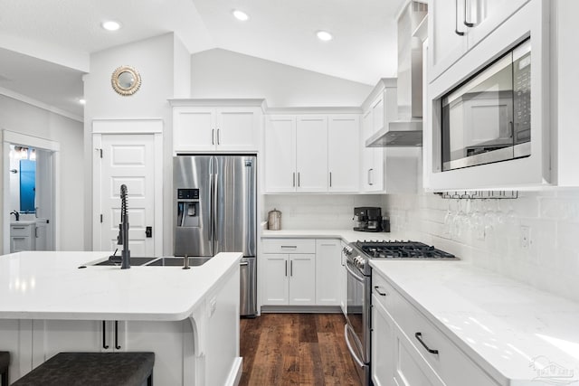 kitchen with dark wood finished floors, appliances with stainless steel finishes, white cabinets, wall chimney range hood, and lofted ceiling