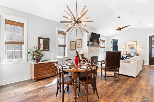 dining area featuring baseboards, lofted ceiling, ceiling fan with notable chandelier, a fireplace, and wood finished floors