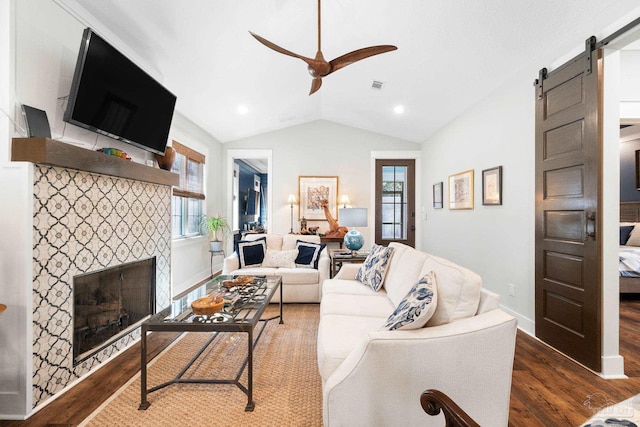 living room featuring visible vents, wood finished floors, a barn door, lofted ceiling, and a tile fireplace