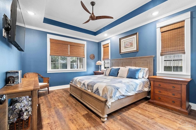 bedroom with recessed lighting, a tray ceiling, baseboards, and wood finished floors