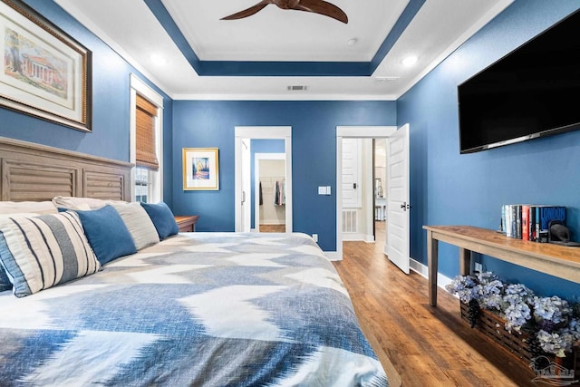 bedroom featuring a tray ceiling, wood finished floors, visible vents, and baseboards