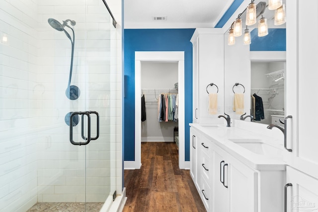 bathroom with a spacious closet, a stall shower, wood finished floors, and a sink