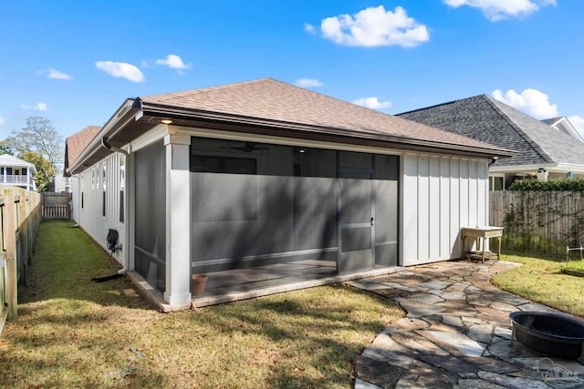 rear view of property featuring a shingled roof, a lawn, a fenced backyard, a sunroom, and a patio