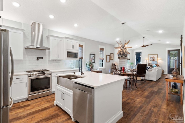 kitchen featuring dark wood finished floors, lofted ceiling, appliances with stainless steel finishes, wall chimney exhaust hood, and open floor plan