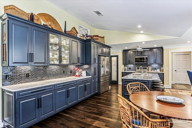 kitchen featuring dark wood-style flooring, vaulted ceiling, visible vents, an island with sink, and appliances with stainless steel finishes