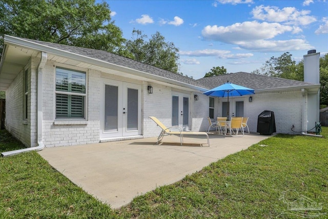 rear view of house featuring french doors, a chimney, brick siding, a patio area, and a yard