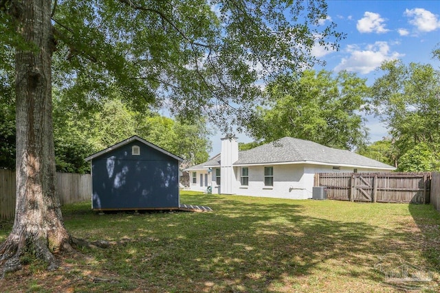 rear view of property with a fenced backyard, a chimney, a yard, and central AC unit