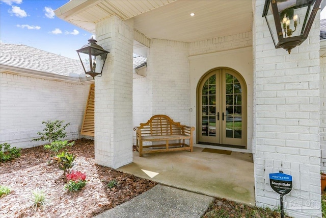 entrance to property featuring a shingled roof, french doors, and brick siding