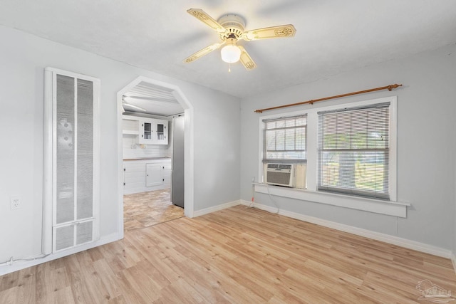 empty room with cooling unit, arched walkways, light wood-type flooring, a ceiling fan, and baseboards