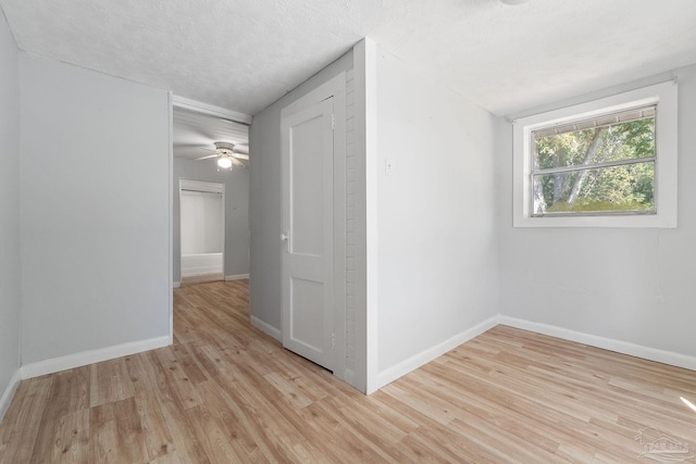 spare room with light wood-type flooring, baseboards, a ceiling fan, and a textured ceiling