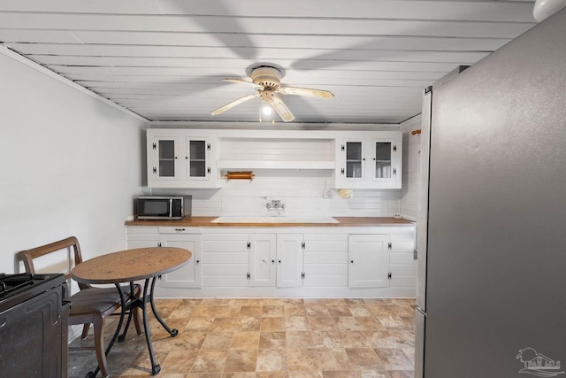 kitchen featuring glass insert cabinets, butcher block counters, white cabinetry, stainless steel microwave, and a sink