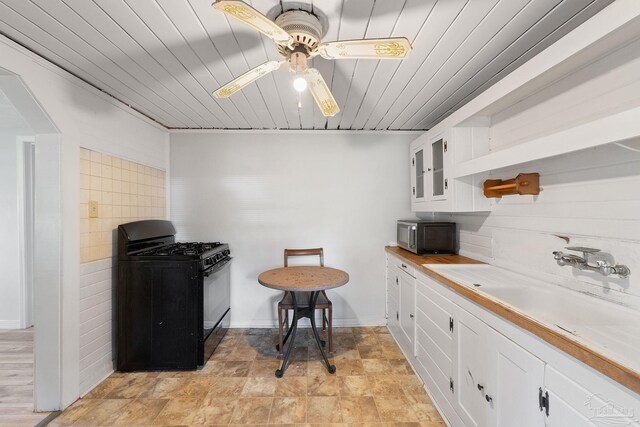 kitchen featuring white cabinetry, wooden ceiling, ceiling fan, gas stove, and sink