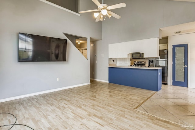 kitchen with kitchen peninsula, ceiling fan, white cabinetry, a towering ceiling, and stainless steel appliances