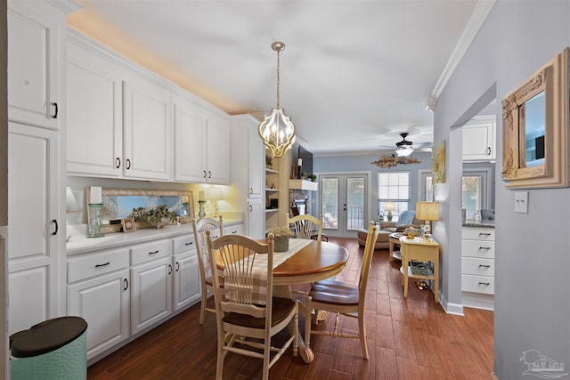 dining area featuring ceiling fan with notable chandelier, dark wood-type flooring, ornamental molding, and french doors