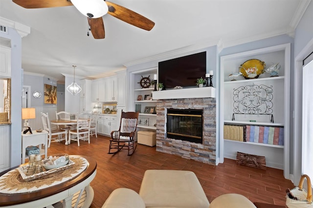 living room featuring ceiling fan, built in features, ornamental molding, wood-type flooring, and a fireplace