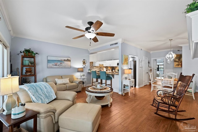 living room with ceiling fan with notable chandelier, ornamental molding, and hardwood / wood-style flooring