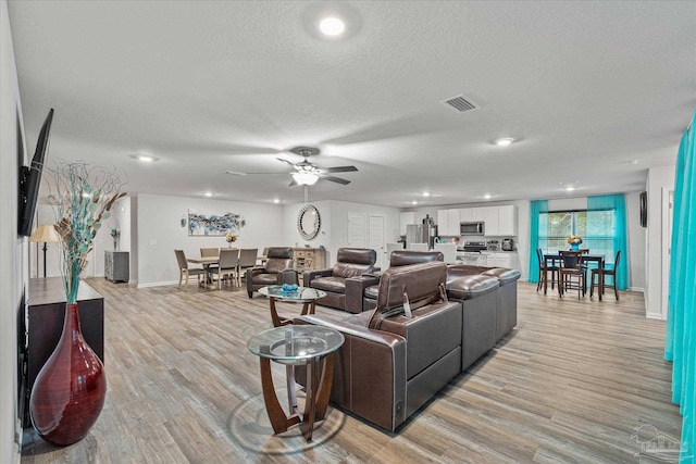 living room featuring ceiling fan, a textured ceiling, and light hardwood / wood-style flooring