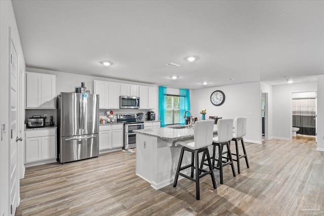 kitchen featuring light stone countertops, white cabinets, stainless steel appliances, an island with sink, and a breakfast bar